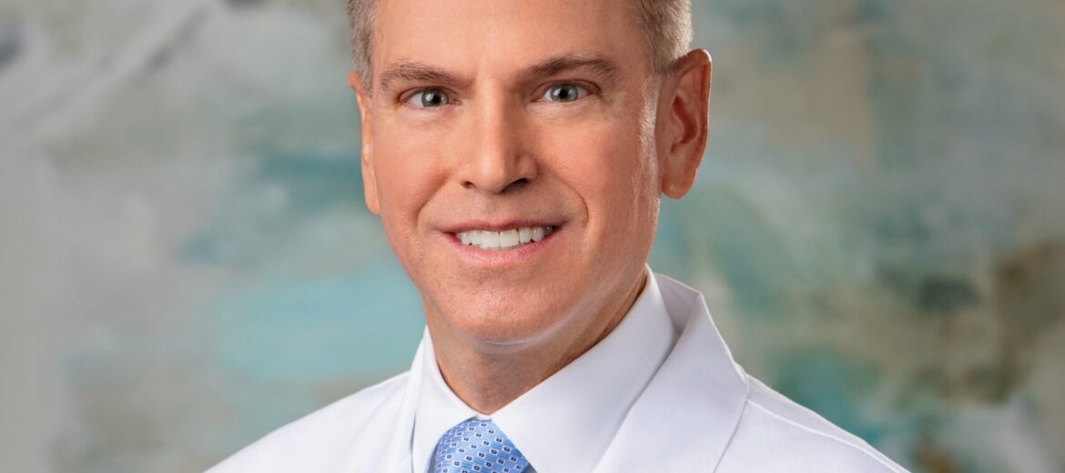 Professional portrait of a smiling male doctor in a white coat.