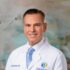 Professional portrait of a smiling male doctor in a white coat.