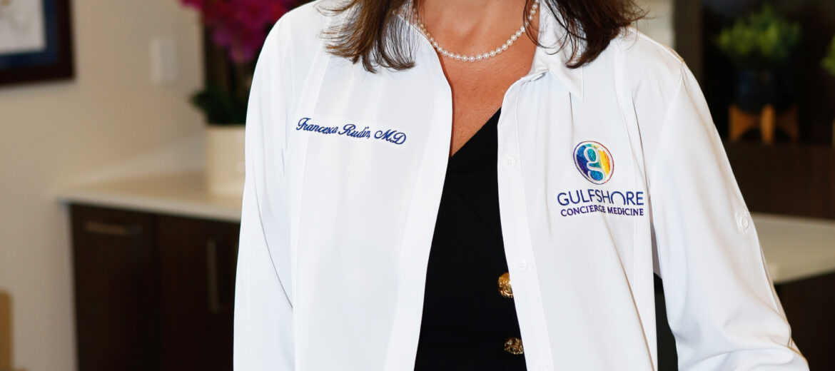 A smiling female doctor in a white coat standing indoors.
