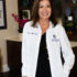 A smiling female doctor in a white coat standing indoors.