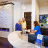 Two elderly men talking to a receptionist at a curved counter.
